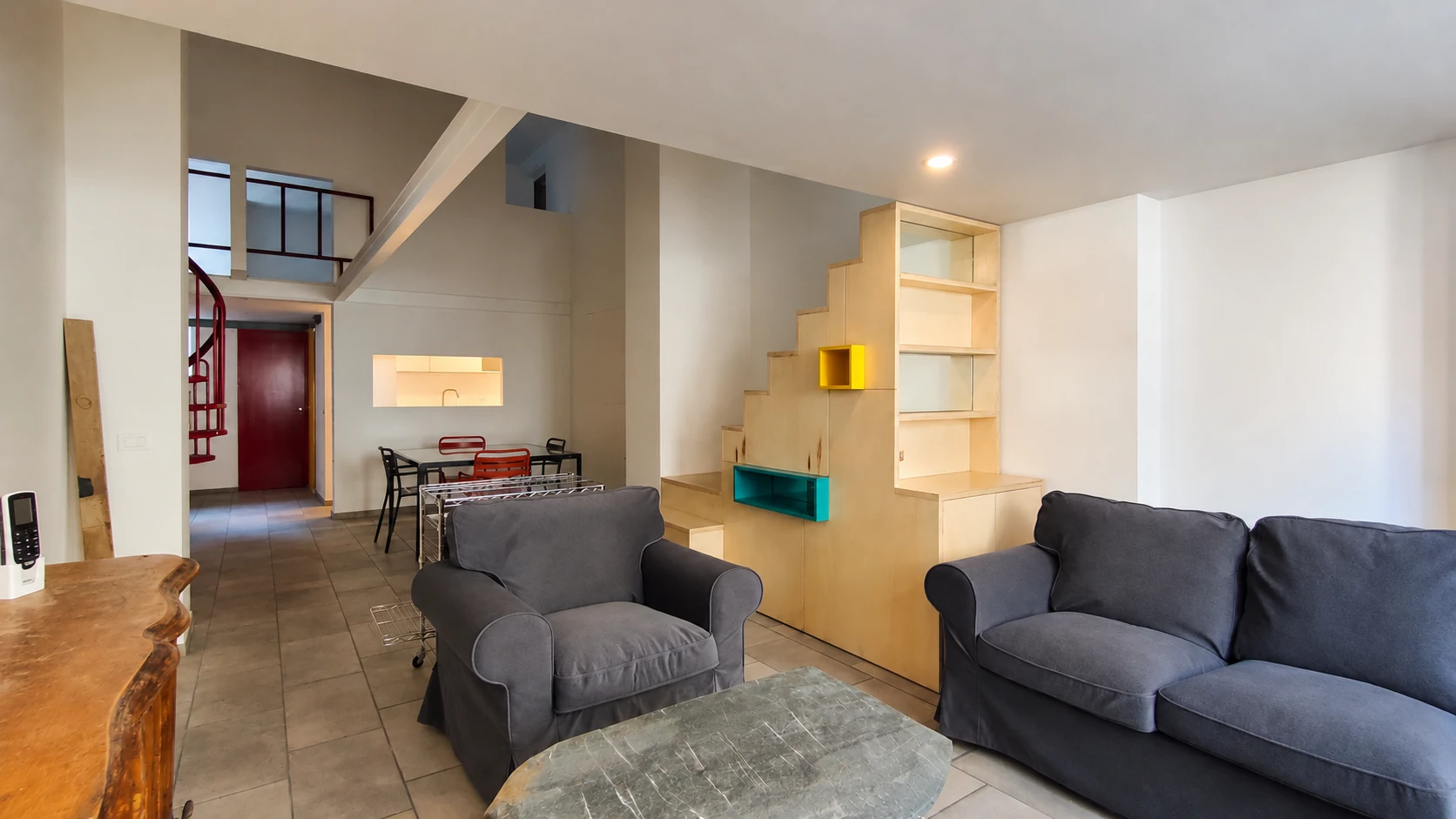 Vista frontale del soggiorno con tavolino in pietra, credenza in legno e due scale di accesso al soppalco.
