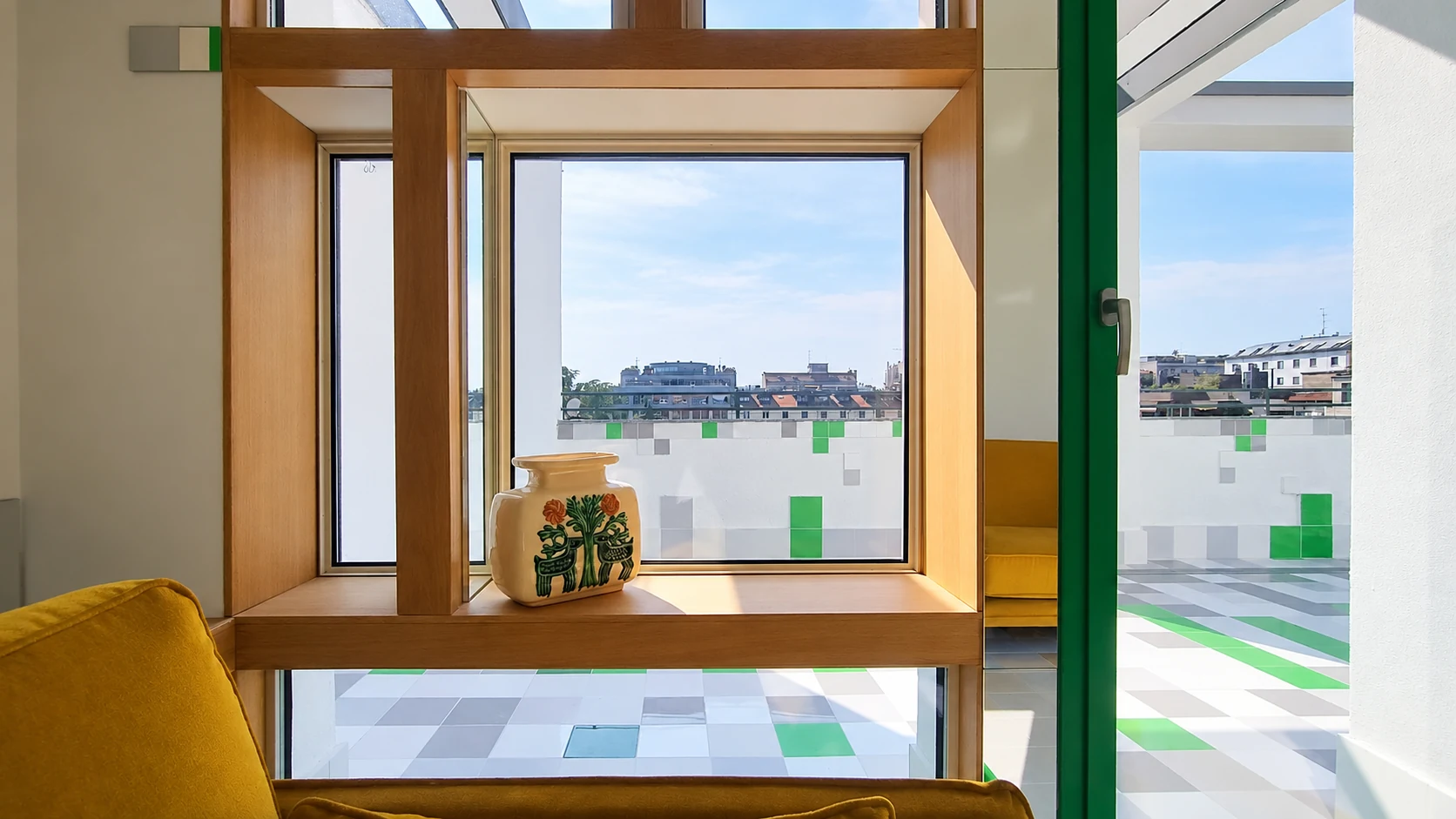 Finestra incorniciata in legno con vaso decorato, affacciata sulla terrazza e sui tetti di Milano