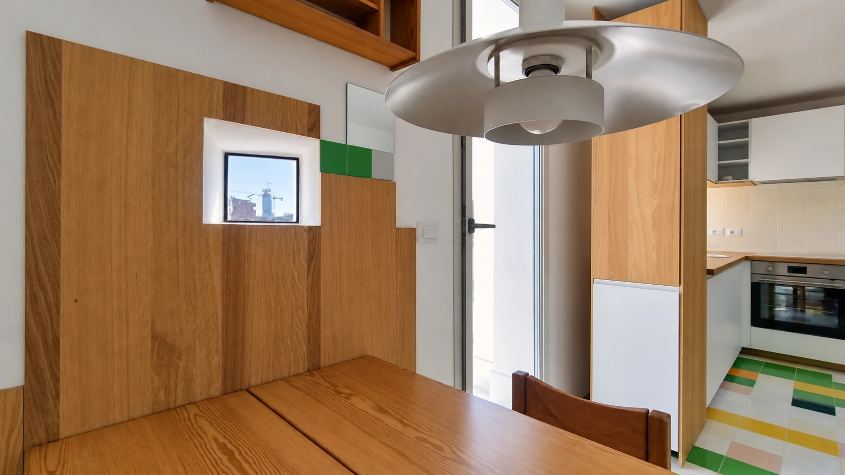 Dettaglio della lampada sospesa e della boiserie in legno nella zona pranzo, con una piccola apertura che incornicia la nuova Torre A2A.